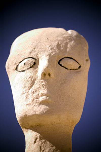 Rostro esculpido claro inclinado hacia arriba, con ojos almendrados dibujados en negro.