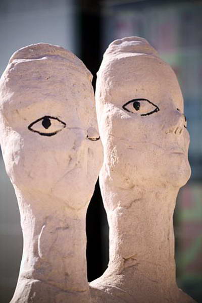Dos cabezas esculpidas alargadas, una junto a otra, con ojos dibujados en negro.