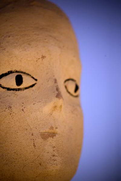 Primerísimo plano de un rostro esculpido, con un ojo dibujado en negro y parte de la nariz.