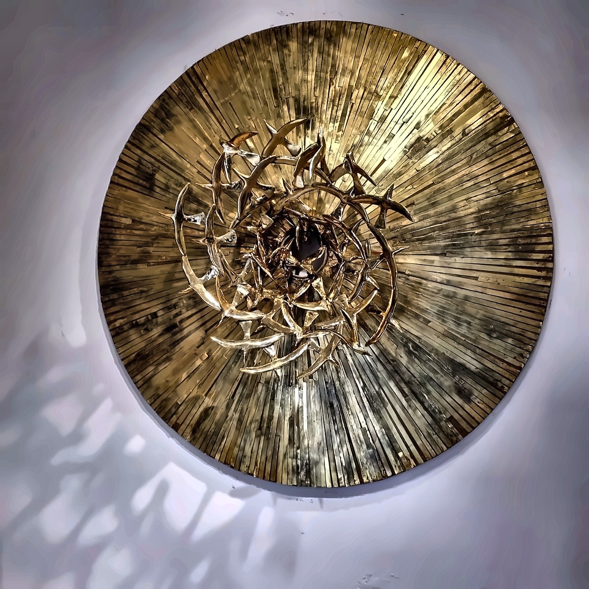 Una obra circular de latón con pájaros que convergen hacia un centro oscuro.