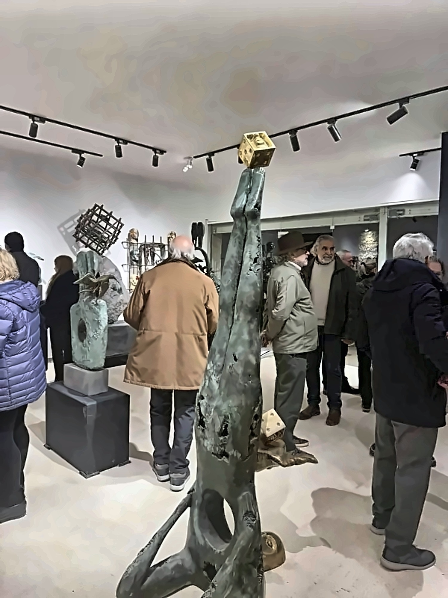A bronze figure holding a gilded cube above its head as visitors gather.
