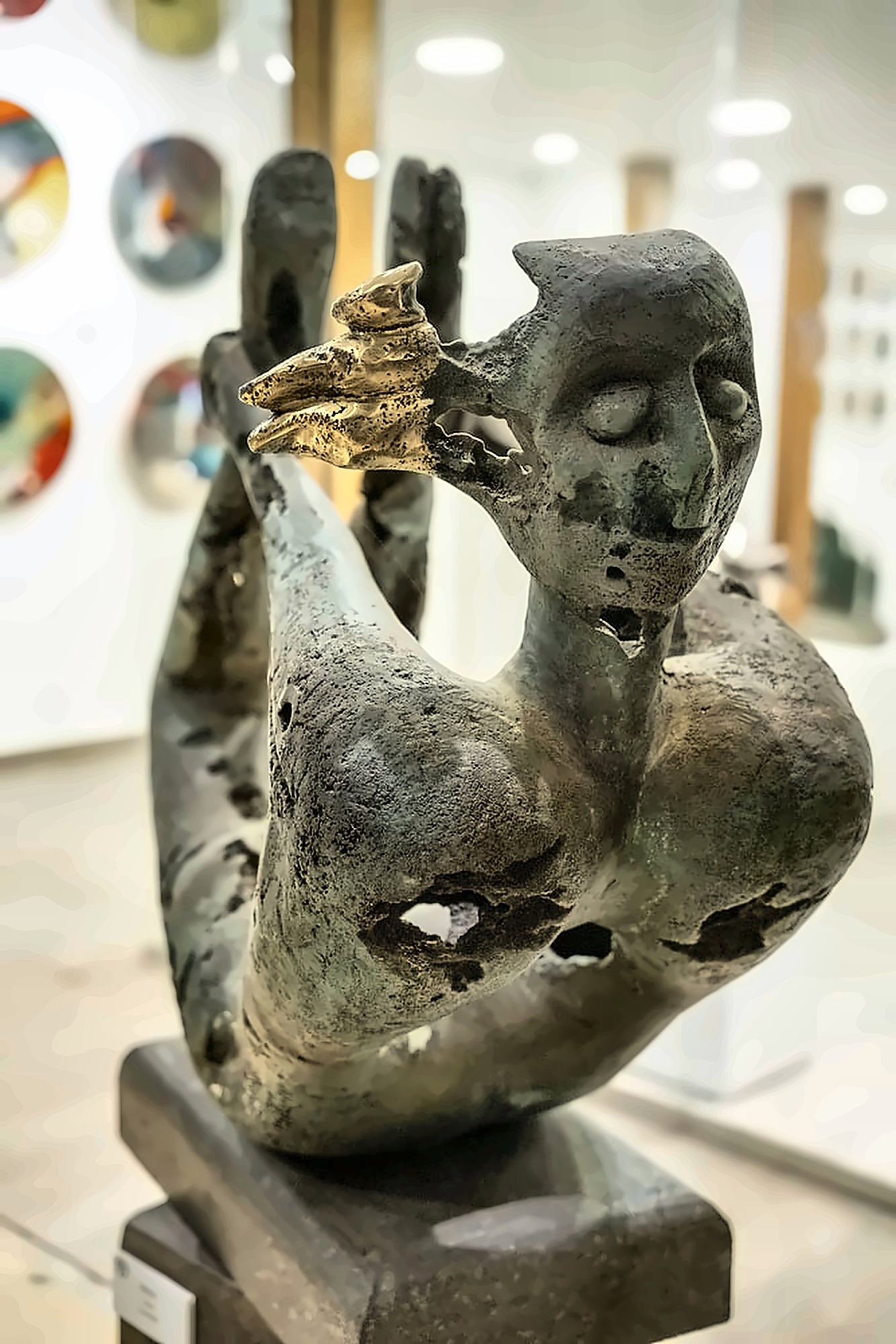 A reclining bronze figure with raised arms, the metal eaten through, a small cluster of gilded birds at the head.