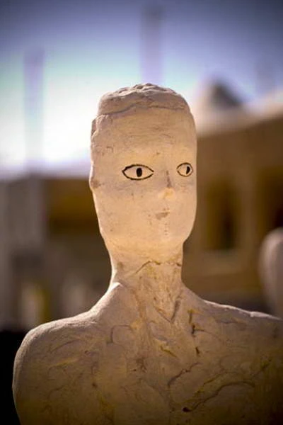 Vista frontal de un rostro esculpido claro y la parte superior del torso, con los ojos dibujados en negro.