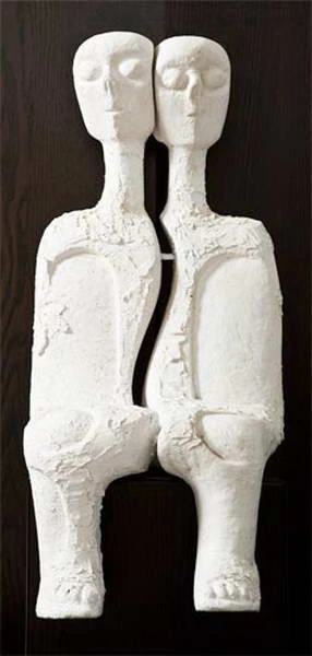 Dos figuras esculpidas claras, unidas lado a lado, con cuellos largos y ojos delineados.