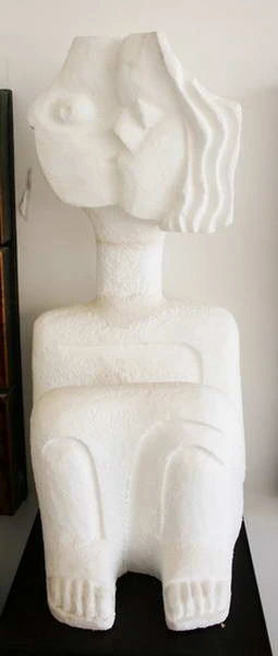 Una figura sentada de yeso blanco, con cabeza estilizada y cabello ondulado.