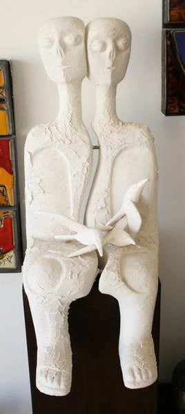 Dos figuras sentadas de yeso blanco que sostienen un pequeño pájaro entre las manos.