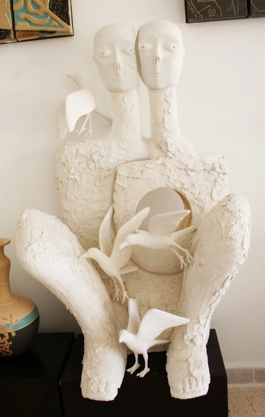Dos figuras sentadas de yeso blanco, con pájaros que salen de una abertura en el pecho.