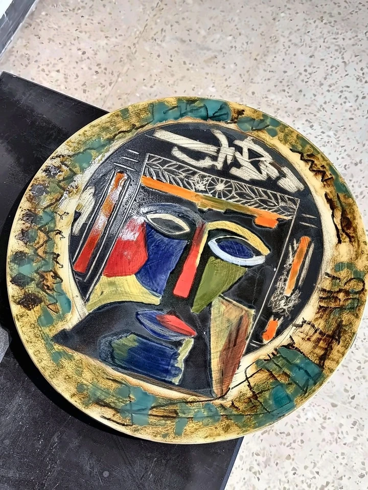 Plato cerámico circular con rostro estilizado, nariz roja y esmaltes azules y amarillos.