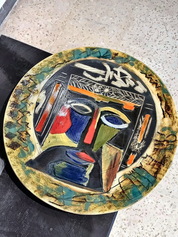 Plato cerámico circular con rostro estilizado, nariz roja y esmaltes azules y amarillos.