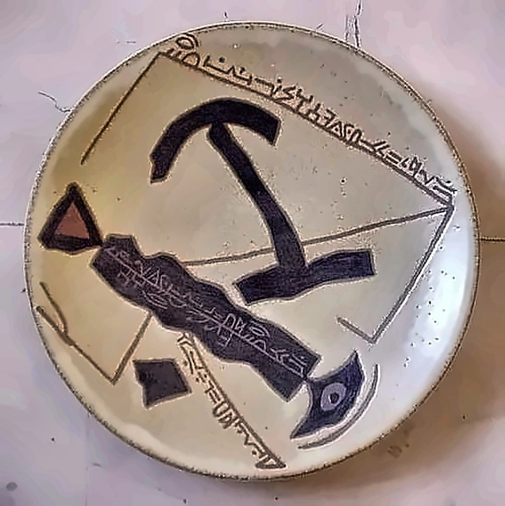 Plato crema con una gran forma negra de ancla y líneas de escritura por el borde y el centro.