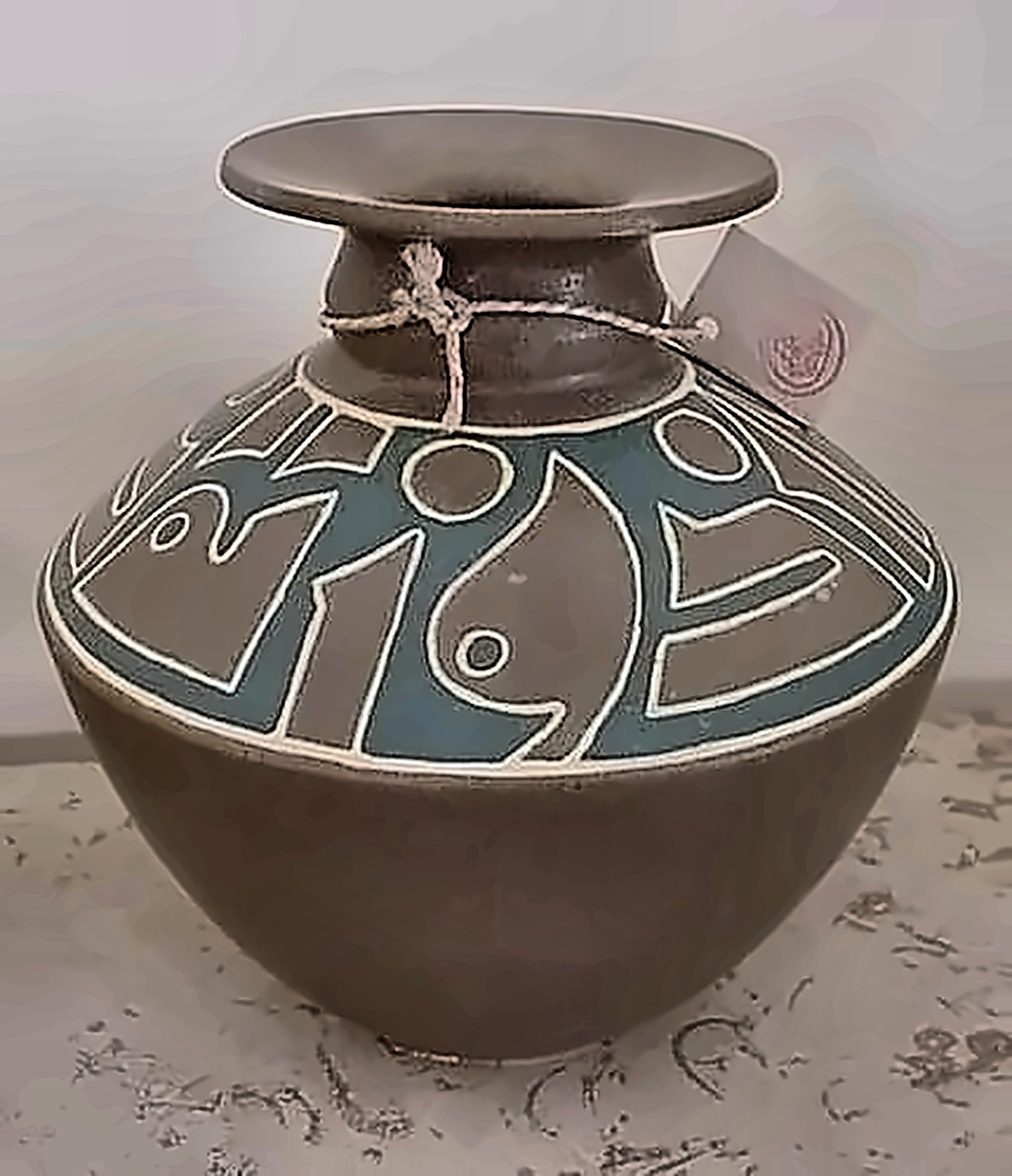 A dark round-bellied jar with a wide flared neck, its shoulder banded in turquoise with pale incised figures.