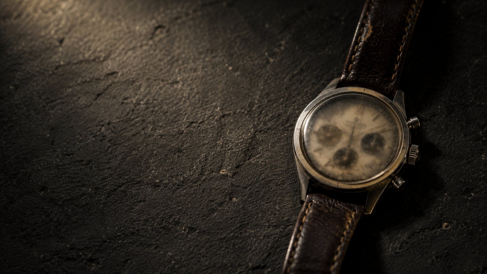 Un viejo reloj de pulsera de acero sobre basalto.